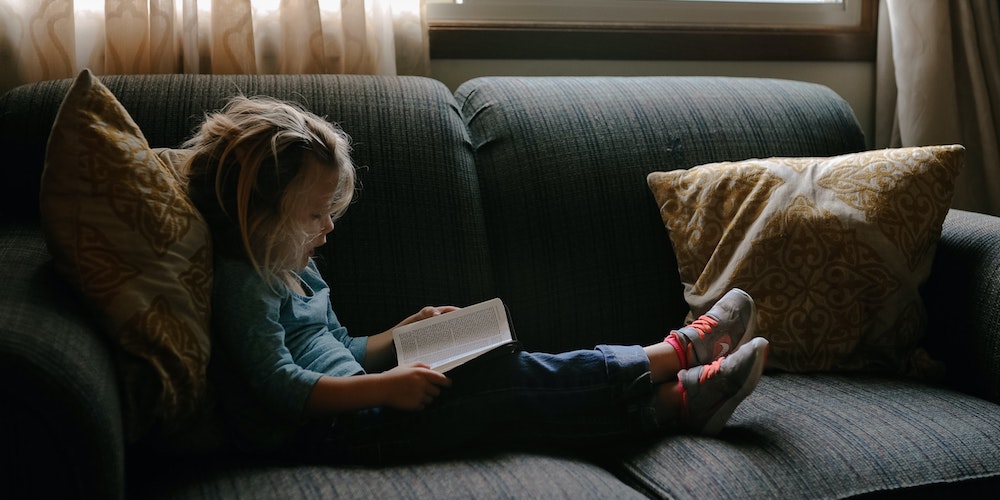 menor leyendo sobre un sofa